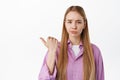Disappointed girl look skeptical, pointing finger left at something lame, bad and uninteresting product, standing Royalty Free Stock Photo