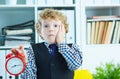 Disappointed kid boss holding a big red alarm clock in his hand suggesting you are late for work. Royalty Free Stock Photo