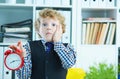 Disappointed kid boss holding a big red alarm clock in his hand suggesting you are late for work. Royalty Free Stock Photo