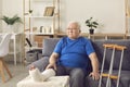 Disappointed senior mature man sitting on sofa with broken leg in cast