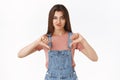 Disappointed skeptical arrogant attractive woman in overalls, t-shirt, smirking unsatisfied, showing thumbs-down and
