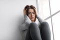 Disappointed upset depressed caucasian young female hold her head with hands sits on windowsill