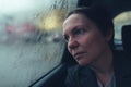 Disappointed and worried businesswoman looking out the window of taxi vehicle on cold rainy day