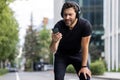 Disappointed young man sportsman runner standing bent and tired on the street wearing headphones and looking upset at