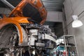 Disassembled orange car in the workshop raised on the lift prepared for repair: front end, hood and bumper removed, internal