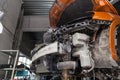 Disassembled orange car in the workshop raised on the lift prepared for repair: front end, hood and bumper removed, internal