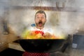 Disaster home cook at kitchen- young funny and desperate man in cooking apron holding pan in flames in stress and fear making a Royalty Free Stock Photo