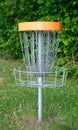 A disc golf basket with chains sits on a grassy field, surrounded by trees Royalty Free Stock Photo