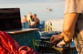 Disc jockey mixing music with his console and laptop on the beach at sunset