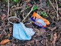 A discarded blue plastic face mask and chocolate bar wrapper against fallen leaves in a rural location in winter in the UK