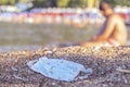 Discarded used face mask lies on a sandy pebble beach, beachgoers are relaxing by the sea in the background. Budva, Montenegro Royalty Free Stock Photo