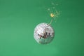 Disco bomb concept. Disco ball with a lit fuse, on green background Royalty Free Stock Photo