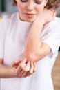 Disconcerted young woman in white t-shirt itching her red elbow Royalty Free Stock Photo