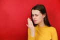 Discontent young brunette woman checking her breath with hand, smells something awful, pinches nose, frowns in displeasure