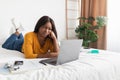 Discontented Black Woman Looking At Laptop Computer Lying In Bedroom Royalty Free Stock Photo