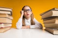 Discontented Schoolgirl Sitting At Table Between Book Stacks, Yellow Background