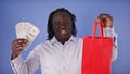 Discount concept. African american black man holding money and shopping bag in his hands. Saving money during the sale Royalty Free Stock Photo