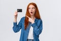 Discounts, shopping and banking concept. Waist-up impressed, thrilled cute redhead girl in denim shirt holding credit