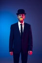 Creative portrait of young stylish man in business suit and bowler hat on his head isolated on dark blue studio