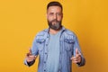 Discreet handsome bearded man weaing light blue t shirt, jeans jacket, showing direction in front of himself with two forefingers Royalty Free Stock Photo