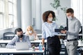 Discussion of colleagues about mistakes in work. Guy and african american woman in protective masks looks at tablet and