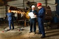 Engineer and worker examine plans near industrial equipment with sparks. Discussion of grab production in factory