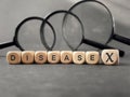 Disease X on wooden blocks with blurry magnifiers in dark background.