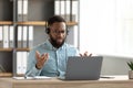 Disgruntled shocked sad young african american bearded male in glasses, headphones gestures and works on pc