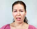 Disgust on a woman`s face, open mouth and sticking tongue, portrait on grey background, emotions series
