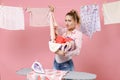 Disgusted displeased young woman housewife in checkered shirt dry clothes on rope and ironing on board hold basin with