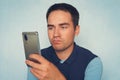 A sad expression on the face of a young man holding a modern smartphone on a blue background Royalty Free Stock Photo