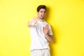 Disgusted man refusing, grimacing from dislike and aversion, begging to stop, standing in white t-shirt against yellow