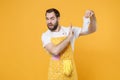 Disgusted puzzled young man househusband in apron doing housework isolated on yellow background studio portrait