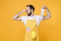 Disgusted young man househusband in apron hold dirty sock while doing housework isolated on yellow background studio