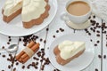 A dish with an appetizing mousse layer (vanilla and chocolate) cake and a cup of milk coffee on a wooden surface