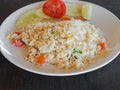 Dish of Asian cuisine - fried white rice with egg, chicken meat and vegetables on a white plate on the wood table in a Thai Royalty Free Stock Photo