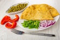 Dish with cheburek, scallion, onion, fork, plate with green peas, pieces of pepper on table
