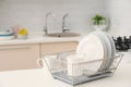 Dish drainer with clean dinnerware on table in kitchen