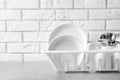 Dish drainer with clean plates on table near brick wall. Royalty Free Stock Photo