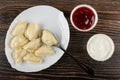 Dish with dumpling and spoon, bowls with strawberry jam and sour cream on wooden table. Top view