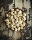 Dish with salted pistachios in a wooden bowl on wooden rustic background, top view