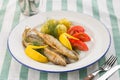 Dish with sardines fried, boiled potatoes, lemon and fresh tomatoes on textile background Royalty Free Stock Photo