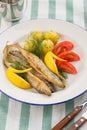 Dish with sardines fried, boiled potatoes, lemon and fresh tomatoes on textile background Royalty Free Stock Photo