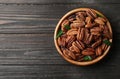 Dish with shelled pecan nuts on wooden background