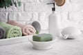 Dish with soap and rolled towels on light table in bathroom