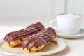 Dish with two eclairs and cup of coffee on white wooden table Royalty Free Stock Photo