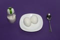 A dish of two eggs with a spoon and salt on a purple background. Royalty Free Stock Photo