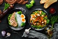 Dishes of chicken meat and vegetables in a black plate on a black background. Buddha bowl. Top view.