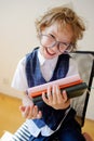 Disheveled little schoolboy holding a stack of textbooks and smiles.