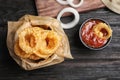 Dishware with homemade crunchy fried onion rings and tomato sauce on wooden table Royalty Free Stock Photo